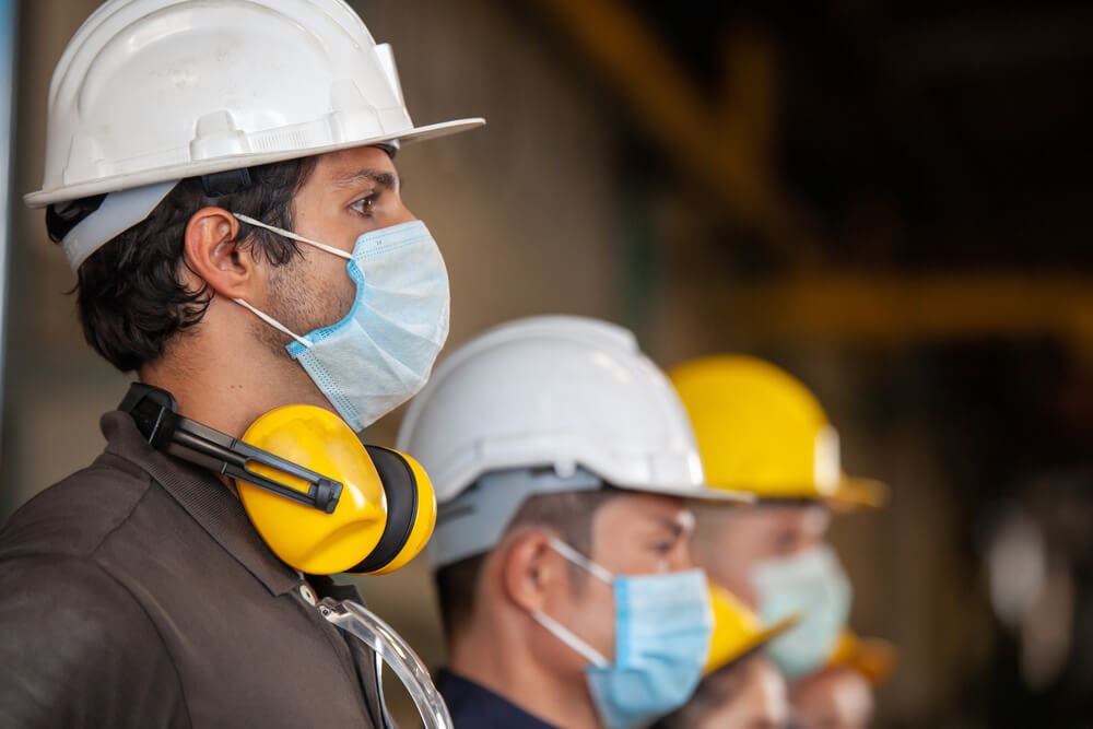 line of construction workers donning masks, hard hats and earmuffs