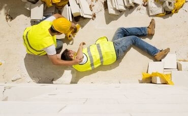 aerial view of construction worker injured on ground with another construction worker tending to him