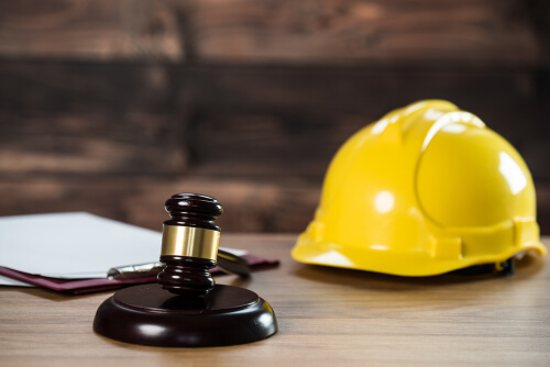 paperwork, judge's gavel, and yellow construction hard hat on a wood surface