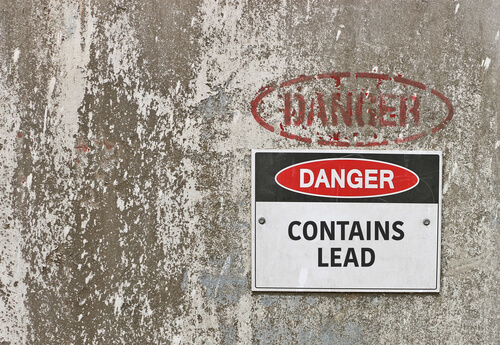 Danger sign that reads 'CONTAINS LEAD' posted to a cement wall
