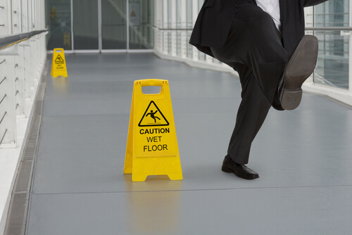 man in business suit slipping on floor next to Caution: Wet Floor sign