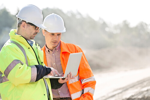 two construction workers looking at a laptop at an outdoor job site