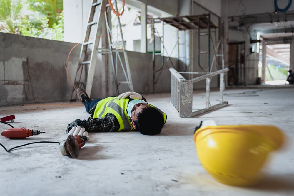 construction worker lying on the ground with overturned ladder next to him and hard hat rolling away in foreground