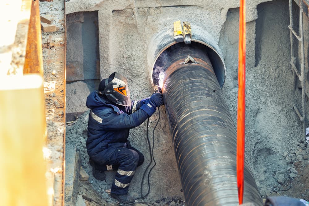 welder in a construction site trench welding a pipe in Jericho, NY