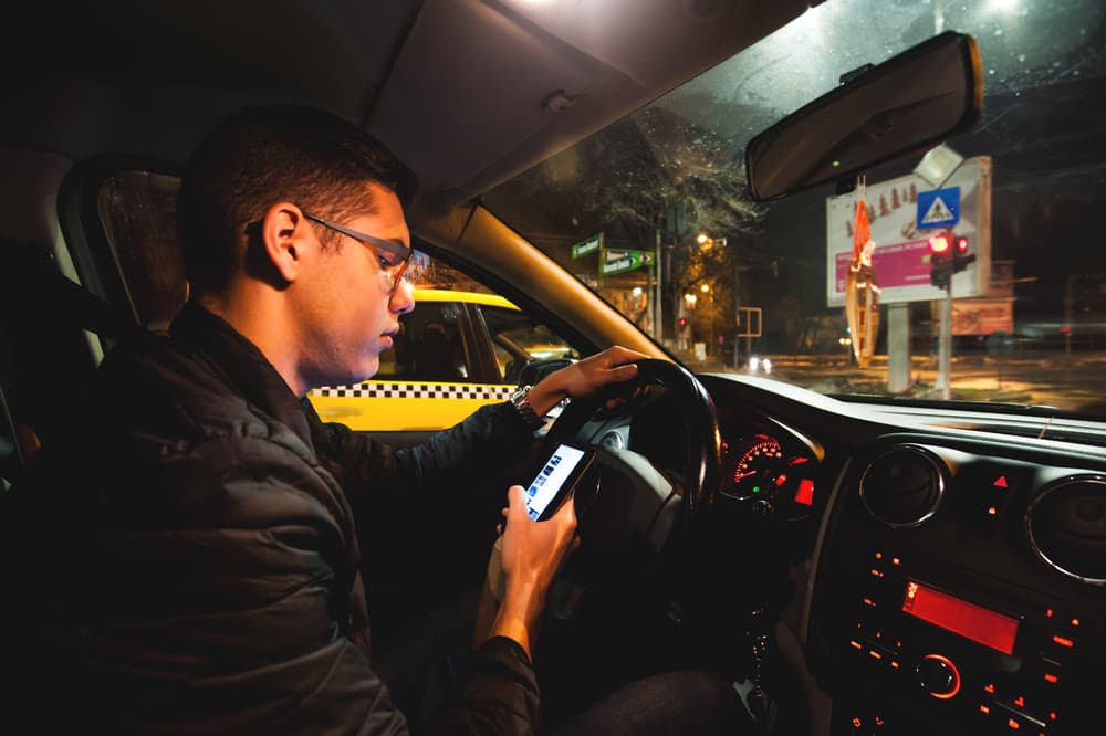 male driver looking down at phone while traveling through a Long Island intersection