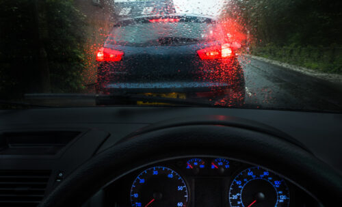 Blurry window from rain, with a car stopped in front of him