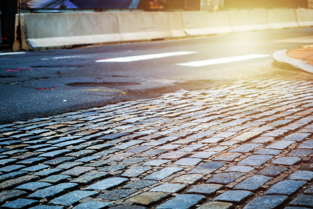 Rough old paving blocks way. Old broken Cobblestone road near the main road.