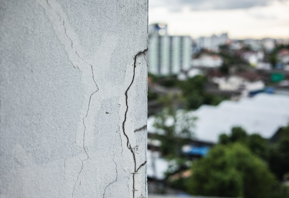 close up shot of cracks on the facade of building with a blurry cityscape in the background