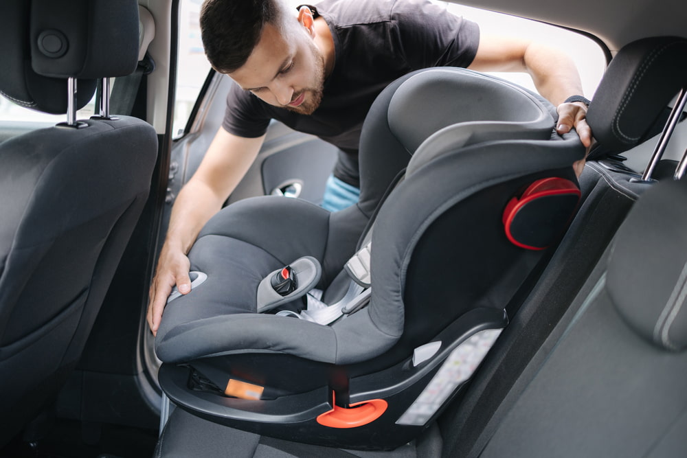 man installing child car seat in the backseat of car with black leather interior