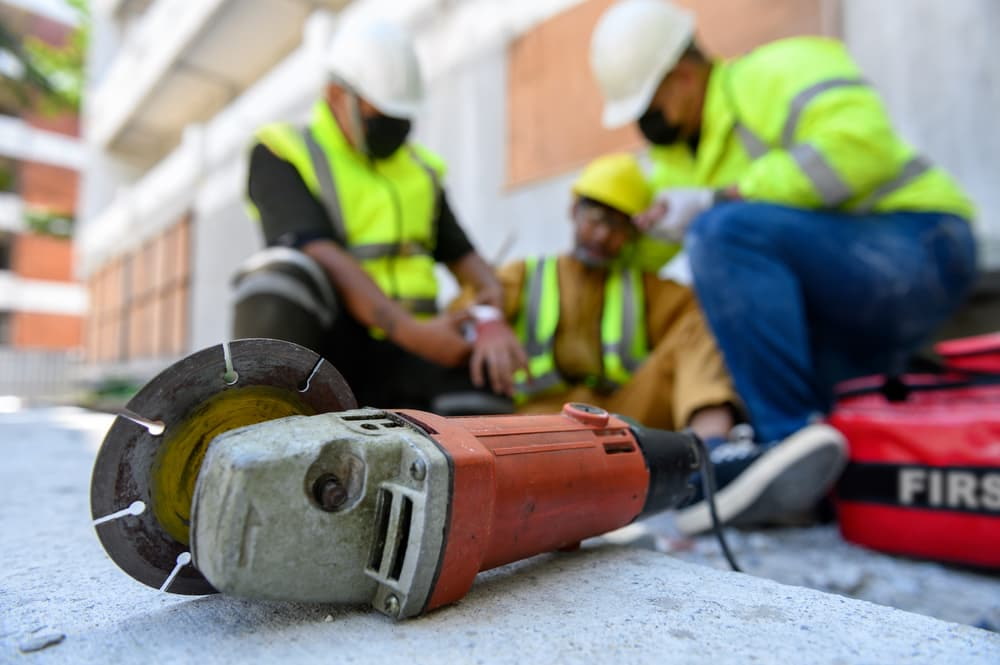 construction power tool on ground with injured construction worker in the background assisted by coworkers