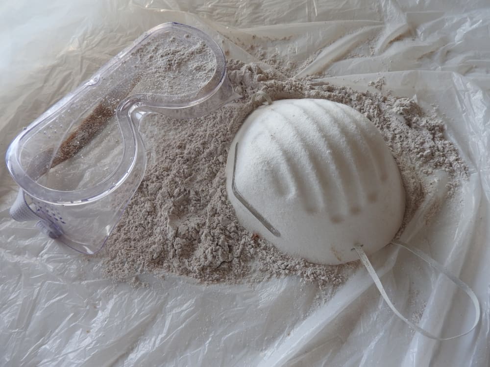 protective mask and goggles laid on sheet covered with plaster dust