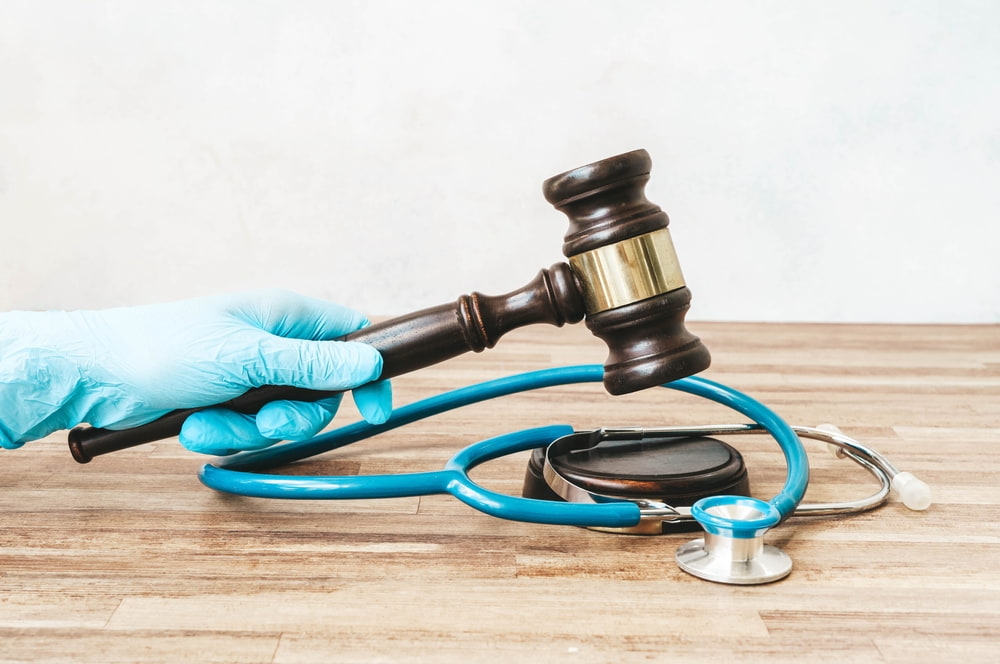 gloved hand banging a gavel on desktop with stethoscope