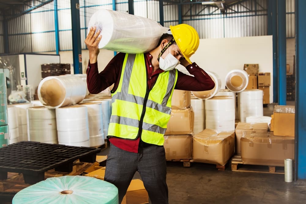 factory worker struggling to lift a heavy object on his shoulders