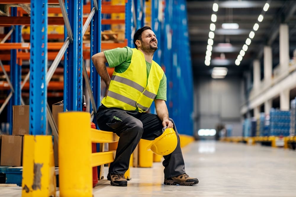 factory worker sitting down holding his injured back wincing in pain