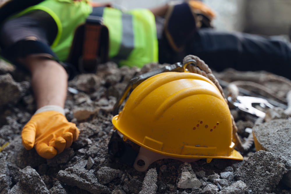 construction worker lying on the ground with hard hat next to him