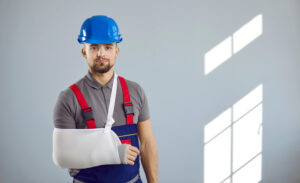 male worker with blue hard hat on and injured arm wrapped in white sling