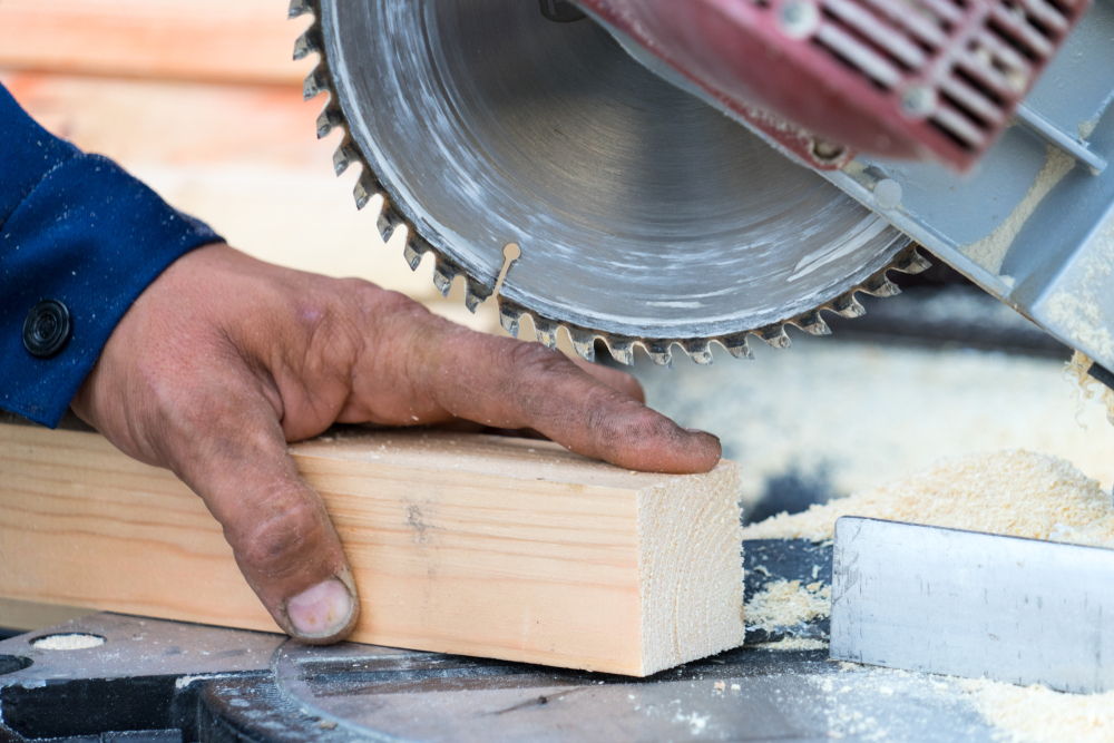 workers hand under a circular saw holding a piece of wood