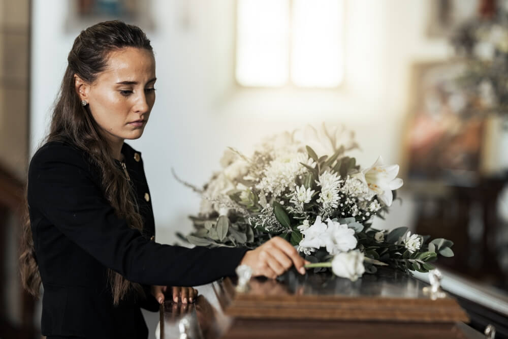 Funeral, sad and woman with flower on coffin after loss of a loved one, family or friend.