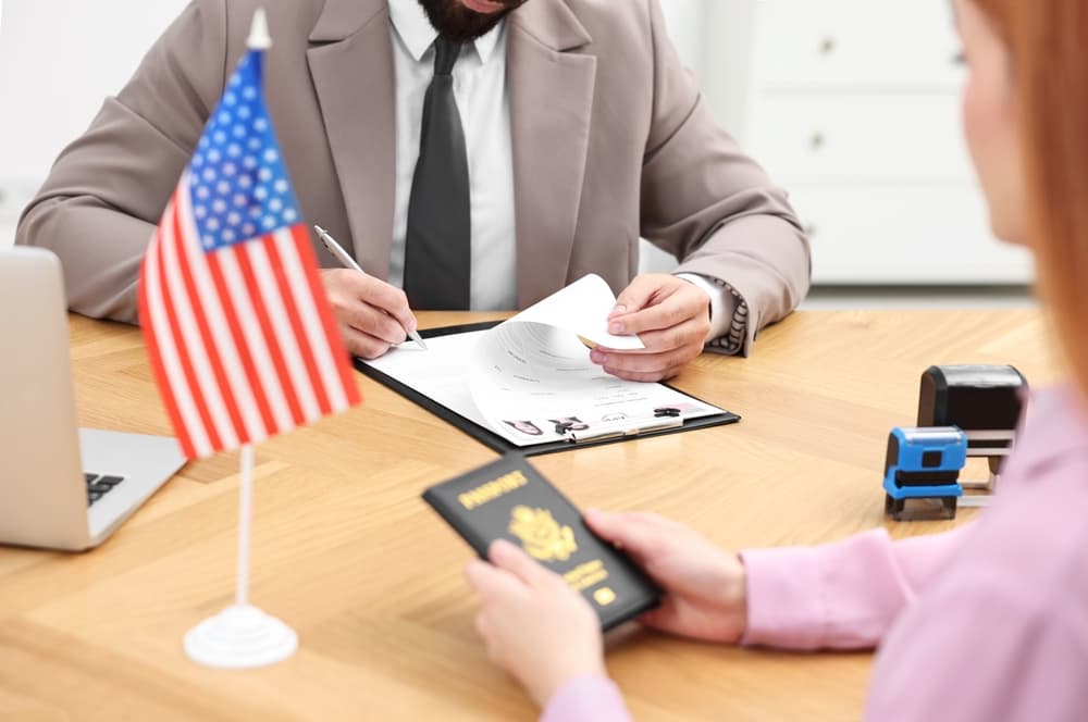 Immigrating to the United States: An embassy officer reviews and approves a woman’s visa application form in an office setting, close-up view.
