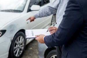 Car accident case The image of an insurance agent examining a car after an accident and writing on a clipboard during the claims process.