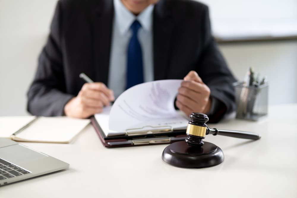A lawyer drafting a legal document at a desk, surrounded by stationery and a laptop, in a relaxed, professional law firm office environment.