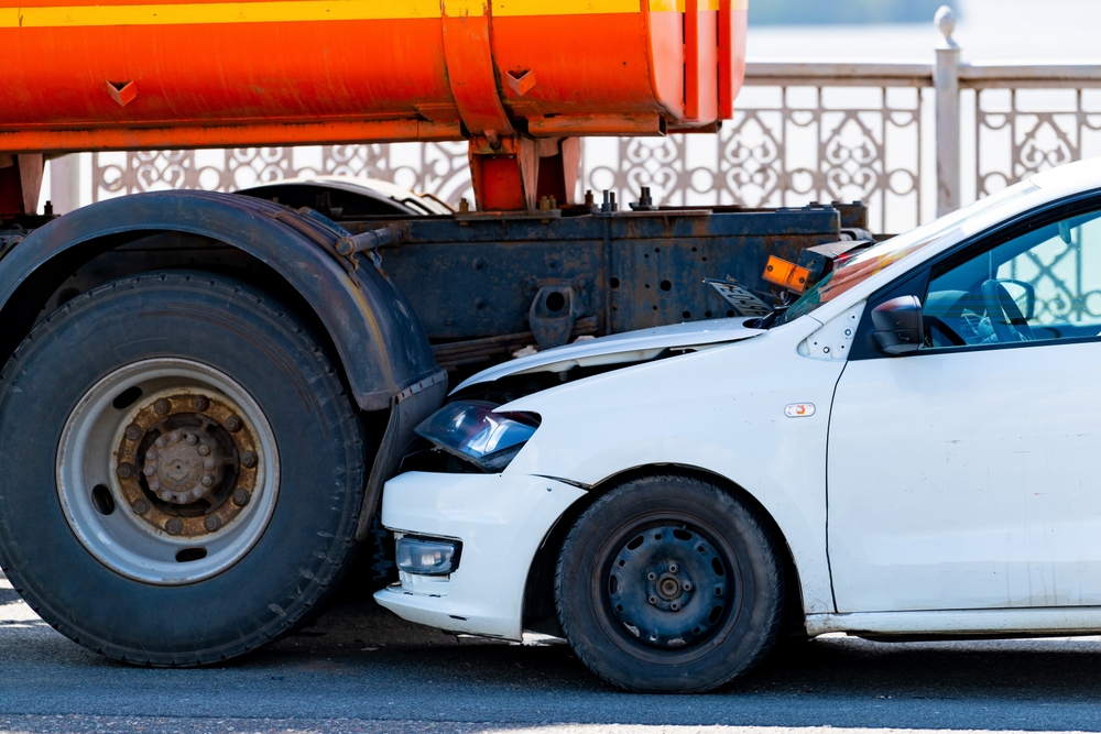 A traffic accident involving two cars and a truck on the road, where one of the cars has collided with the rear end of the truck.