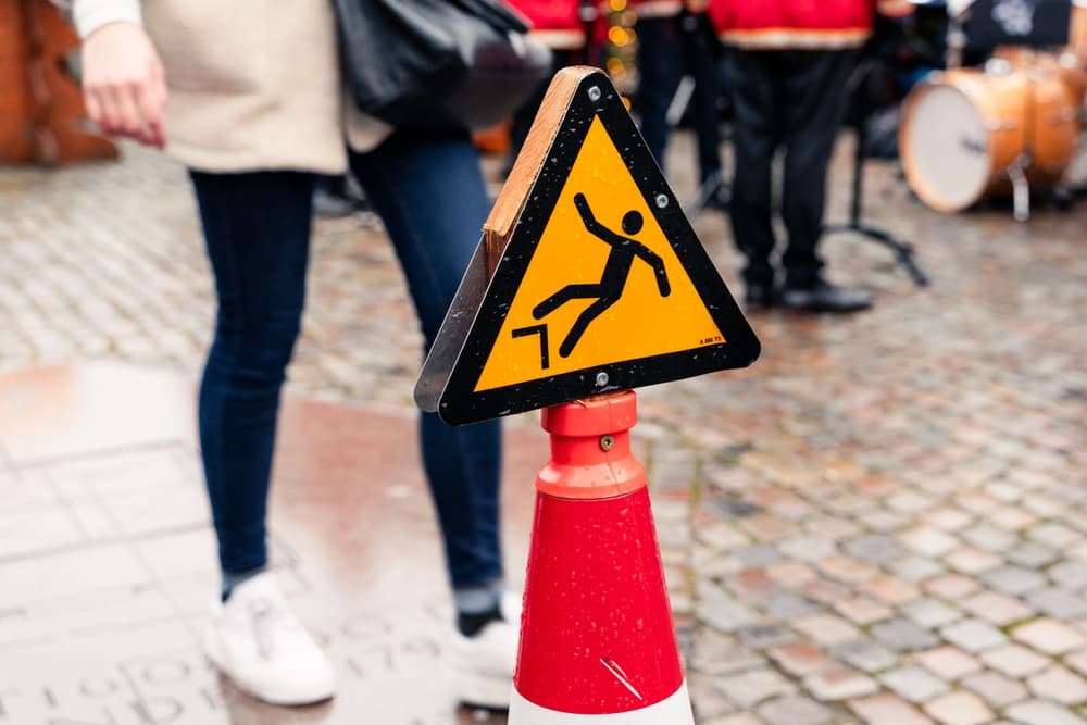 A yellow caution sign warning of a slippery surface stands on a sidewalk, alerting pedestrians to potential hazards ahead.
