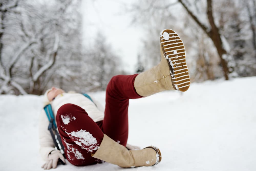A shot capturing the moment a person slips and falls on an icy path in a snowy winter park. The woman lies on the ground, highlighting the risk of seasonal injuries.