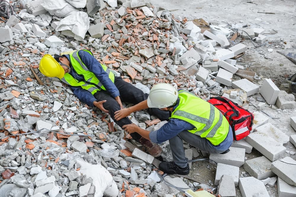 Workplace accident at a construction site: Worker sustains a knee injury after slipping or stumbling on concrete debris. Foreman assists the injured colleague.