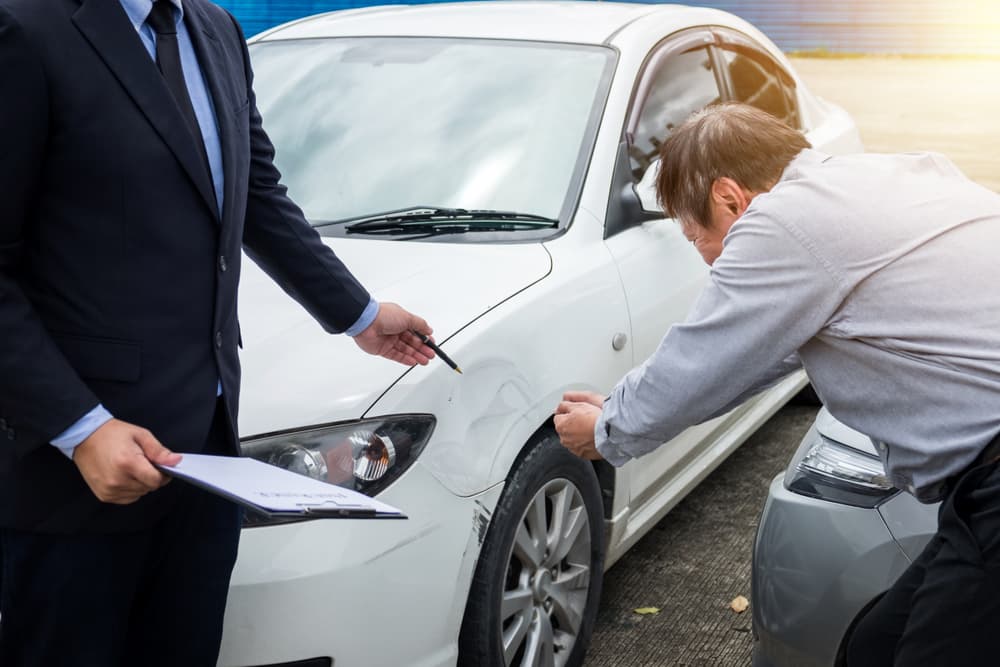 An insurance agent inspects a damaged car and fills out a claim report after a traffic accident, representing the insurance and claims process.