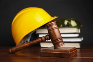 Workplace accident concept: A gavel, legal books, and construction worker's protective gear arranged on a wooden table, symbolizing legal and safety matters.