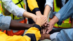 Construction workers joining hands in teamwork and unity at job site.