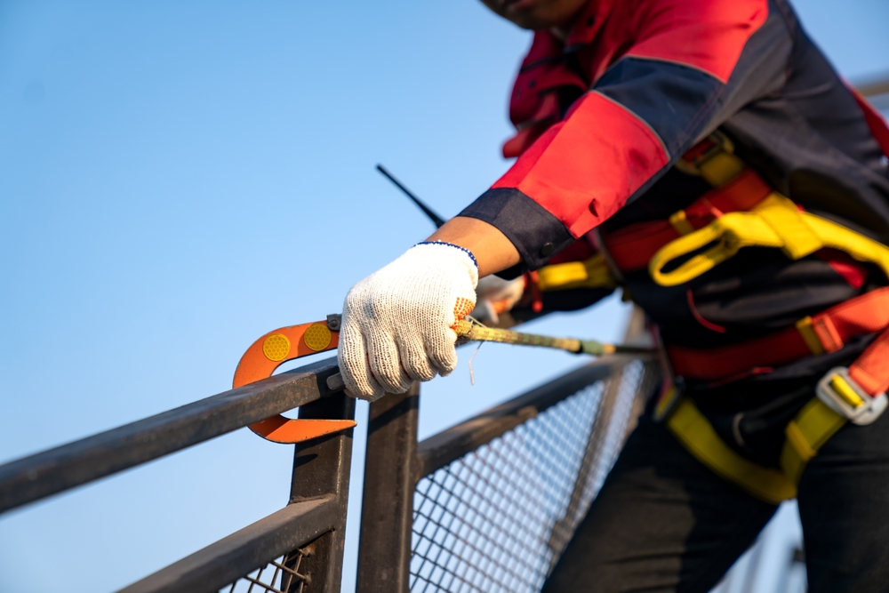 Construction worker using fall protection harness while working at height on a metal railing at a construction site.