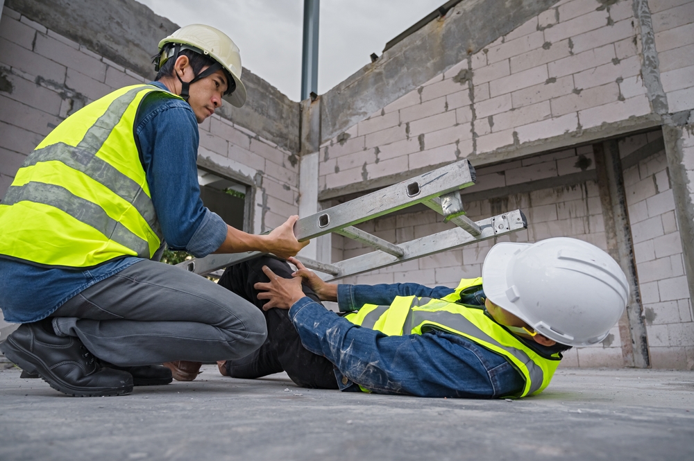 Construction worker assisting an injured coworker on a job site after a workplace accident involving a ladder.