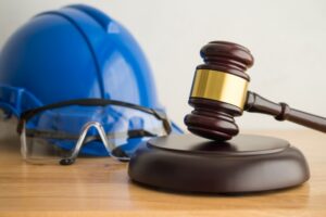 Construction accident lawyers concept with gavel, hard hat, and safety goggles on a work surface.